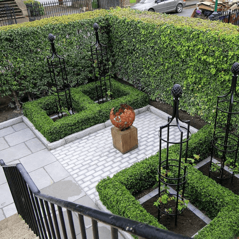 Black metal obelisk trellis on a patio walkway, with rounded finial and lattice sides