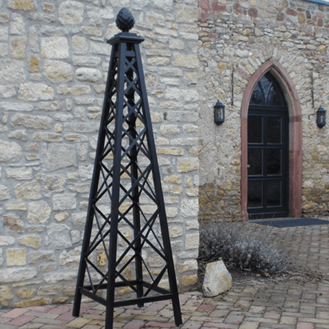 Black metal pyramid garden obelisk against a stone wall near a door