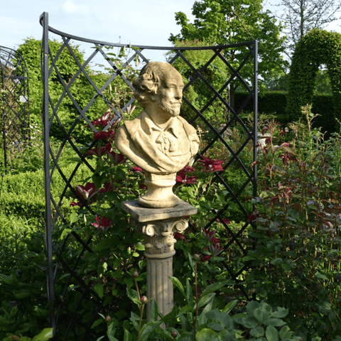 Garden bust sculpture on ornate pedestal, framed by black metal trellis and flowers